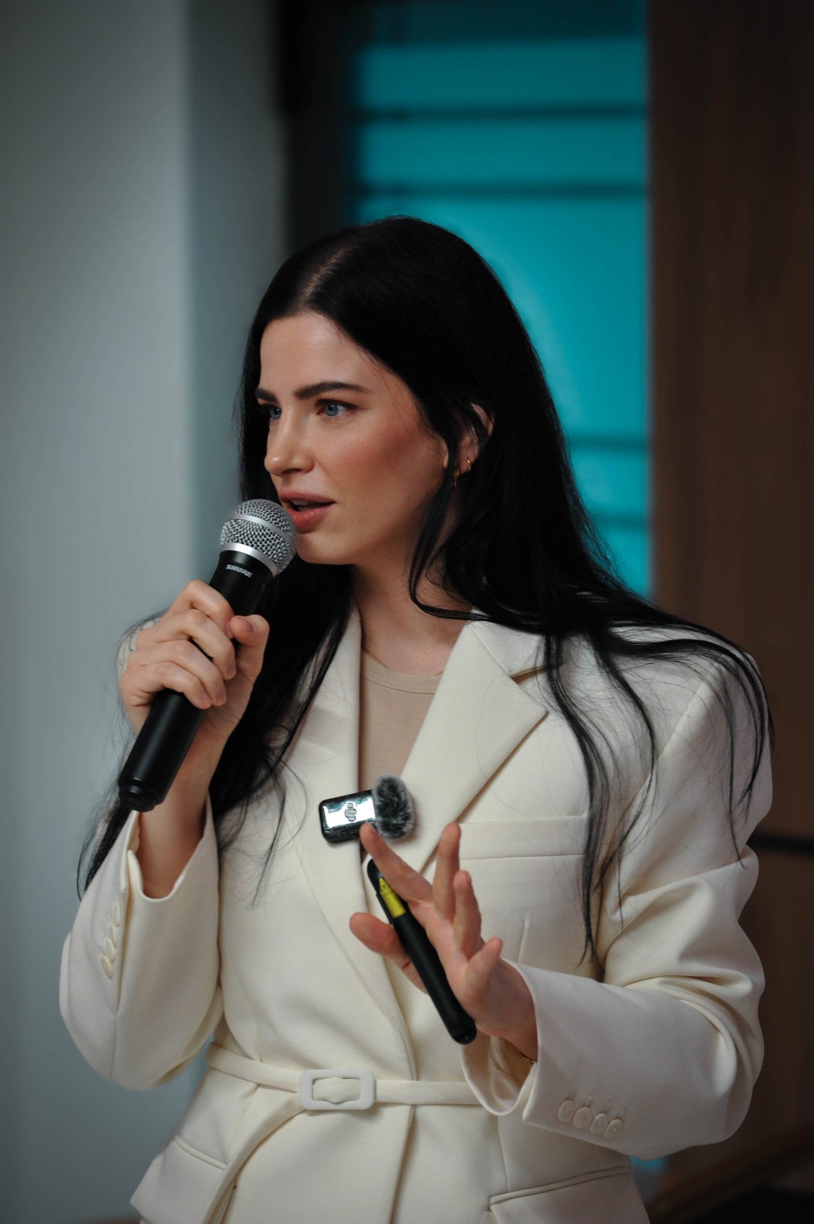 Woman in a white suit holding a microphone and a remote control.
